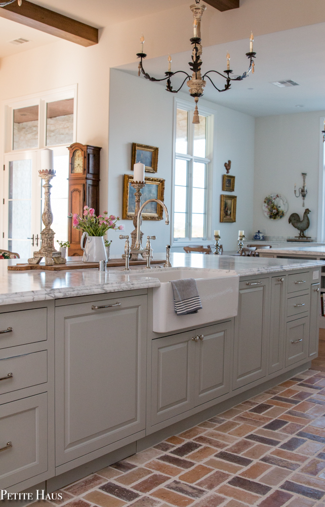 Gorgeous French country kitchen with huge kitchen island painted Benjamin Moore Silver Song, farm sink, and marble countertops. Design by Petite Haus.