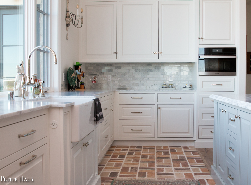 farmhouse kitchen with white cabinets, marble counter and brick floor